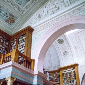 From below of aged building interior with decorative ceiling and walls near collection of literature on bookshelves